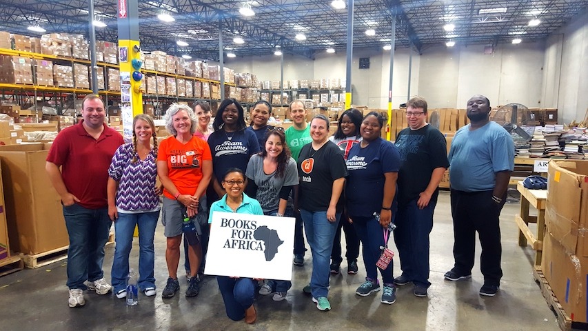 Slide Show Image #2: Group of employees in a wharehouse. One kneels on the floor in front of the group and holds a sign that says "Books for Africa"